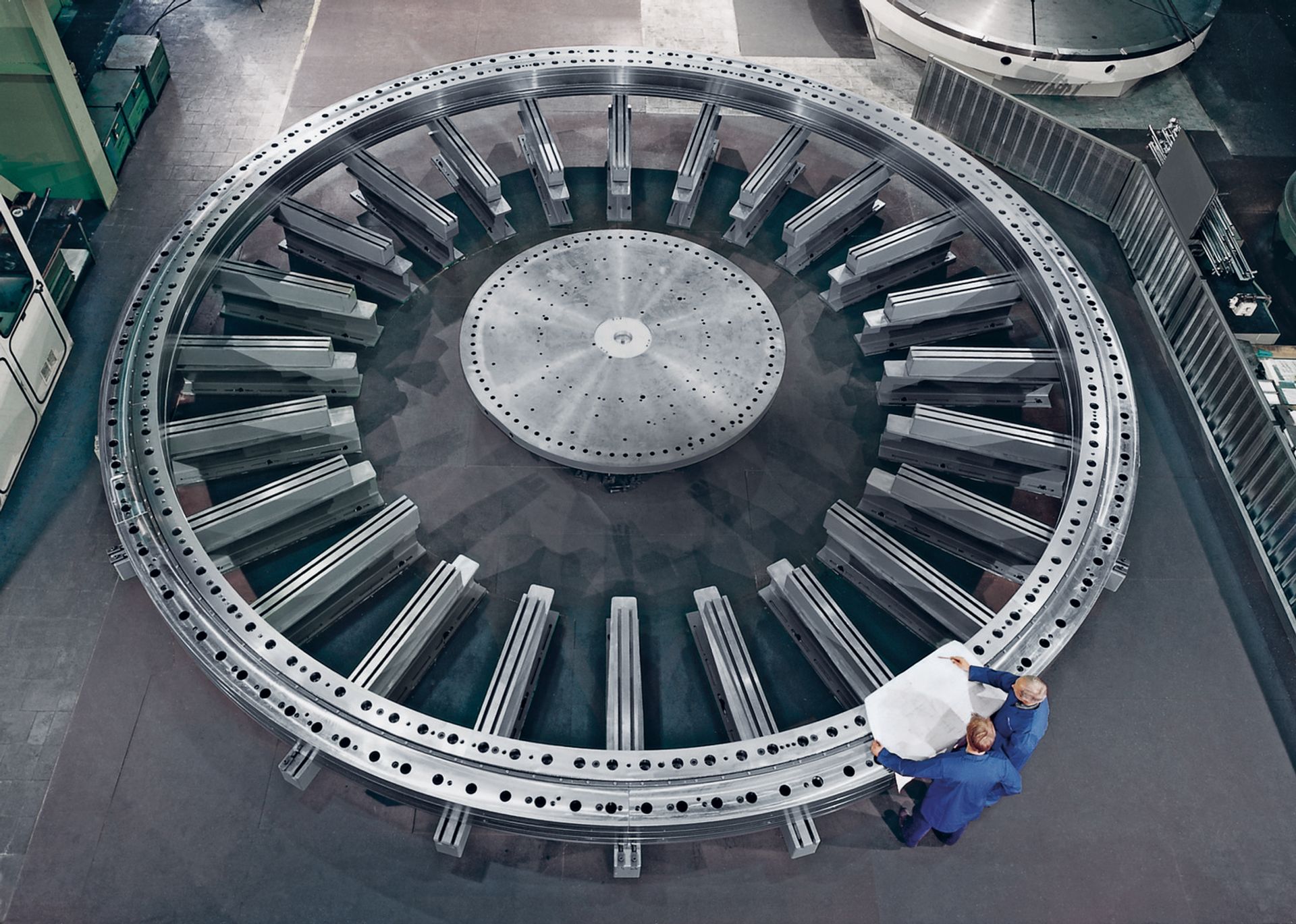 Zwei Fachkräfte von thyssenkrupp rothe erde prüfen anhand technischer Unterlagen ein groß dimensioniertes Großwälzlager in einer Produktionshalle.