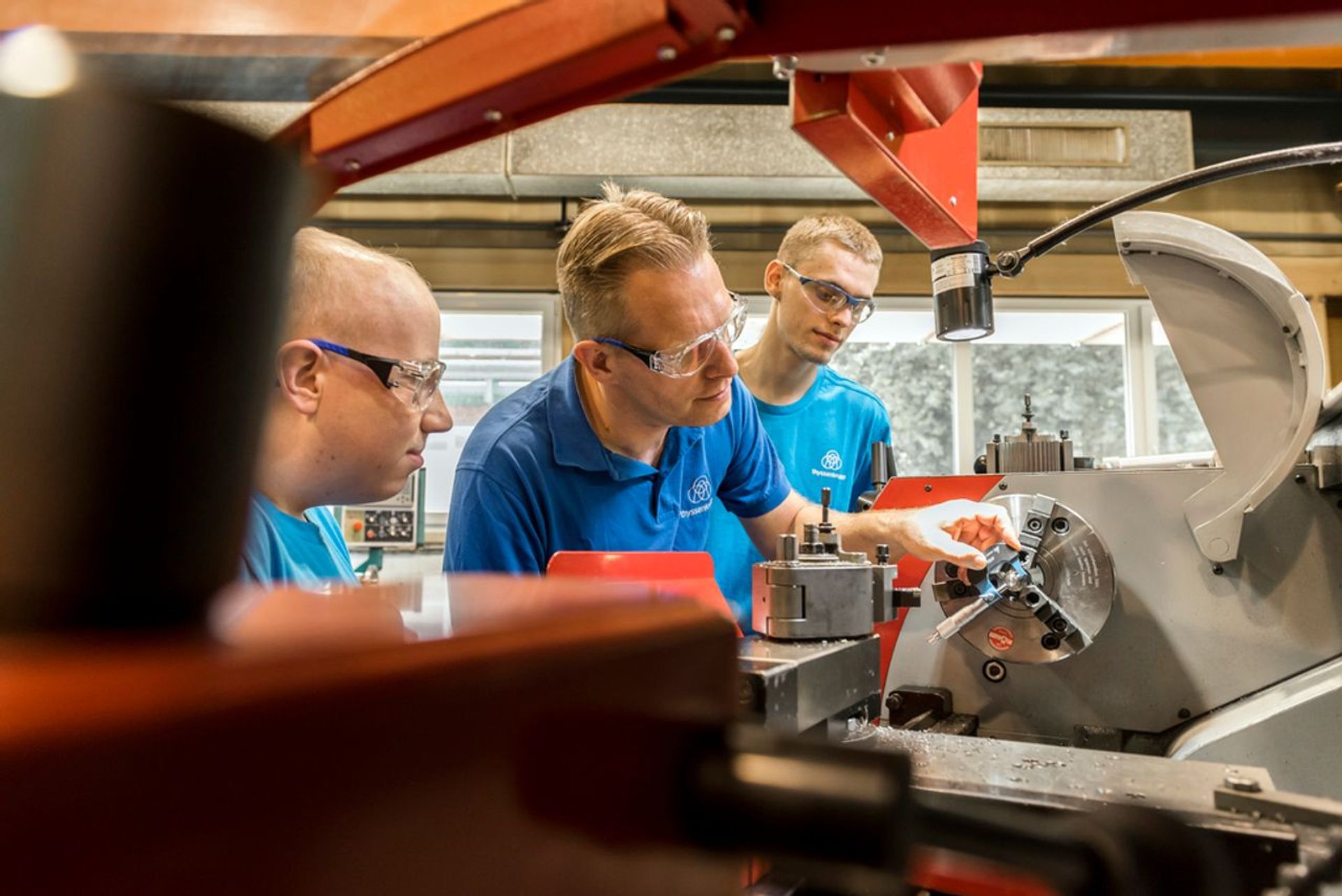 Drei Auszubildende arbeiten gemeinsam an einer Drehmaschine und lernen die präzise Metallbearbeitung im technischen Unterricht
