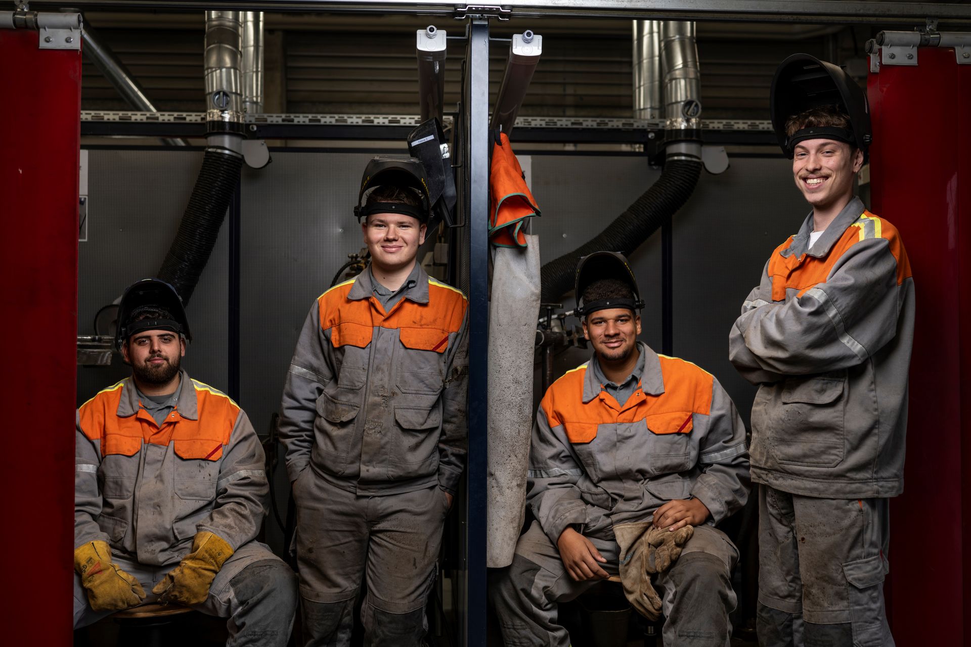 Four people in work and protective clothing sit and stand in a workshop cabin in the technical training area.