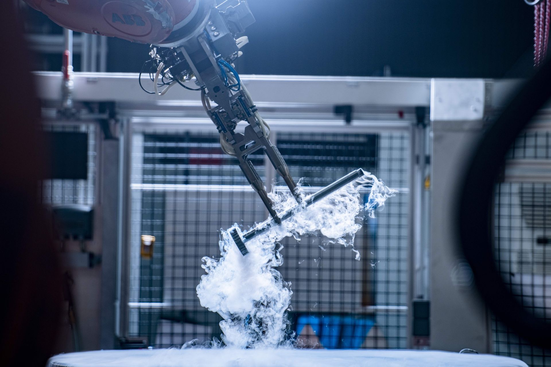 Ein Roboterarm bewegt eine Nockenwelle in einer abgesicherten industriellen Prüfanlage von thyssenkrupp.