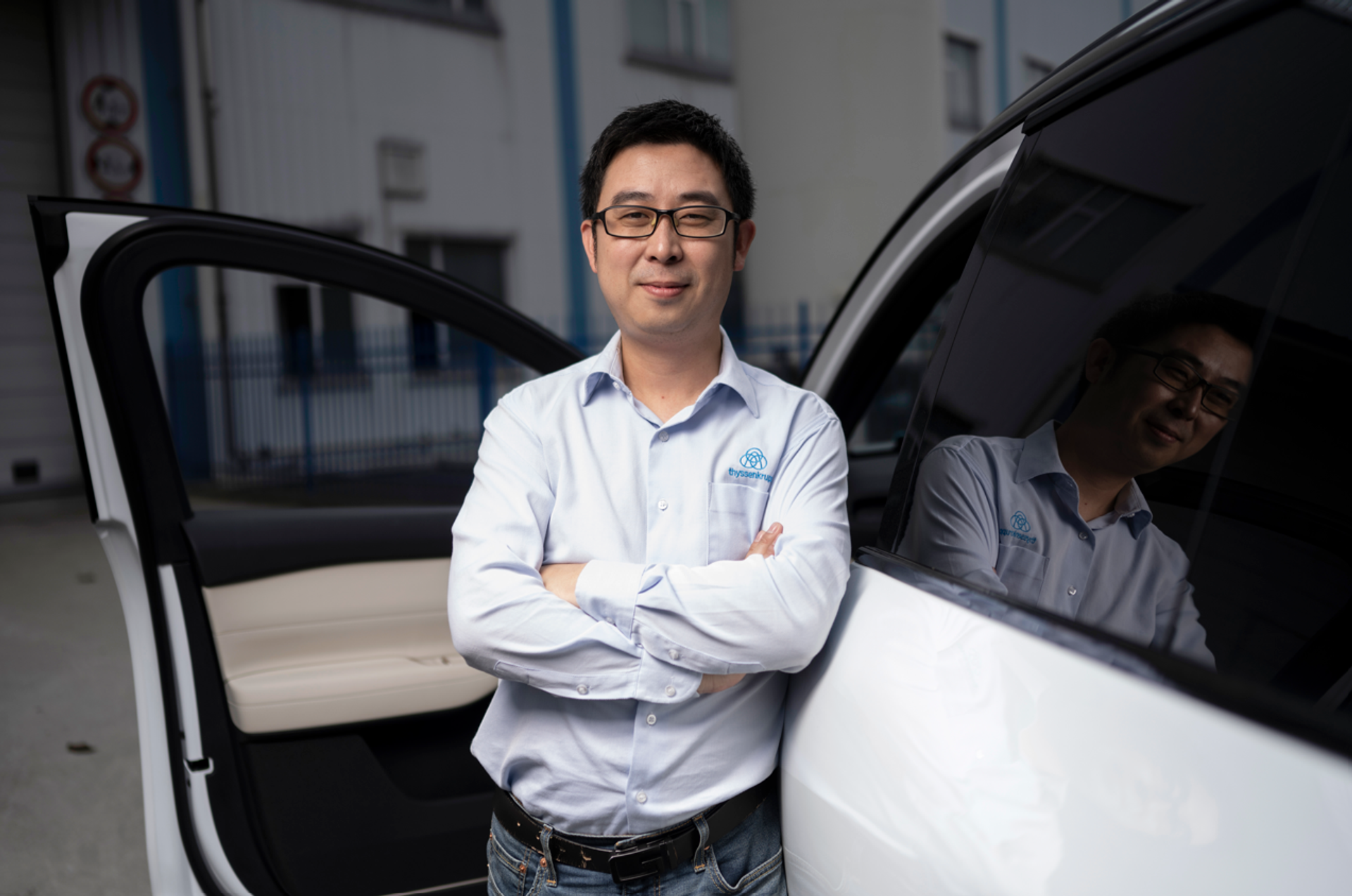 Zhengjie XUE stands in front of an opened car door, arms crossed