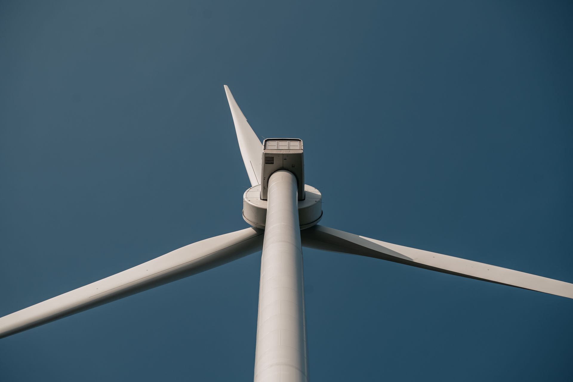 Nahaufnahme einer Windturbine mit drei Rotorblättern, aufgenommen aus der Froschperspektive gegen einen klaren Himmel.
