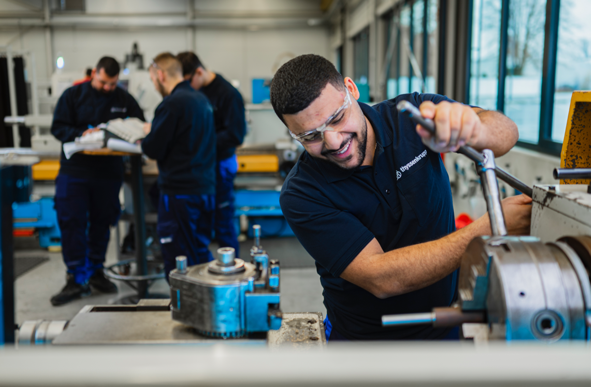 A thyssenkrupp apprentice operates industrial machinery in a training workshop, demonstrating hands-on technical skills and enthusiasm for precision work.