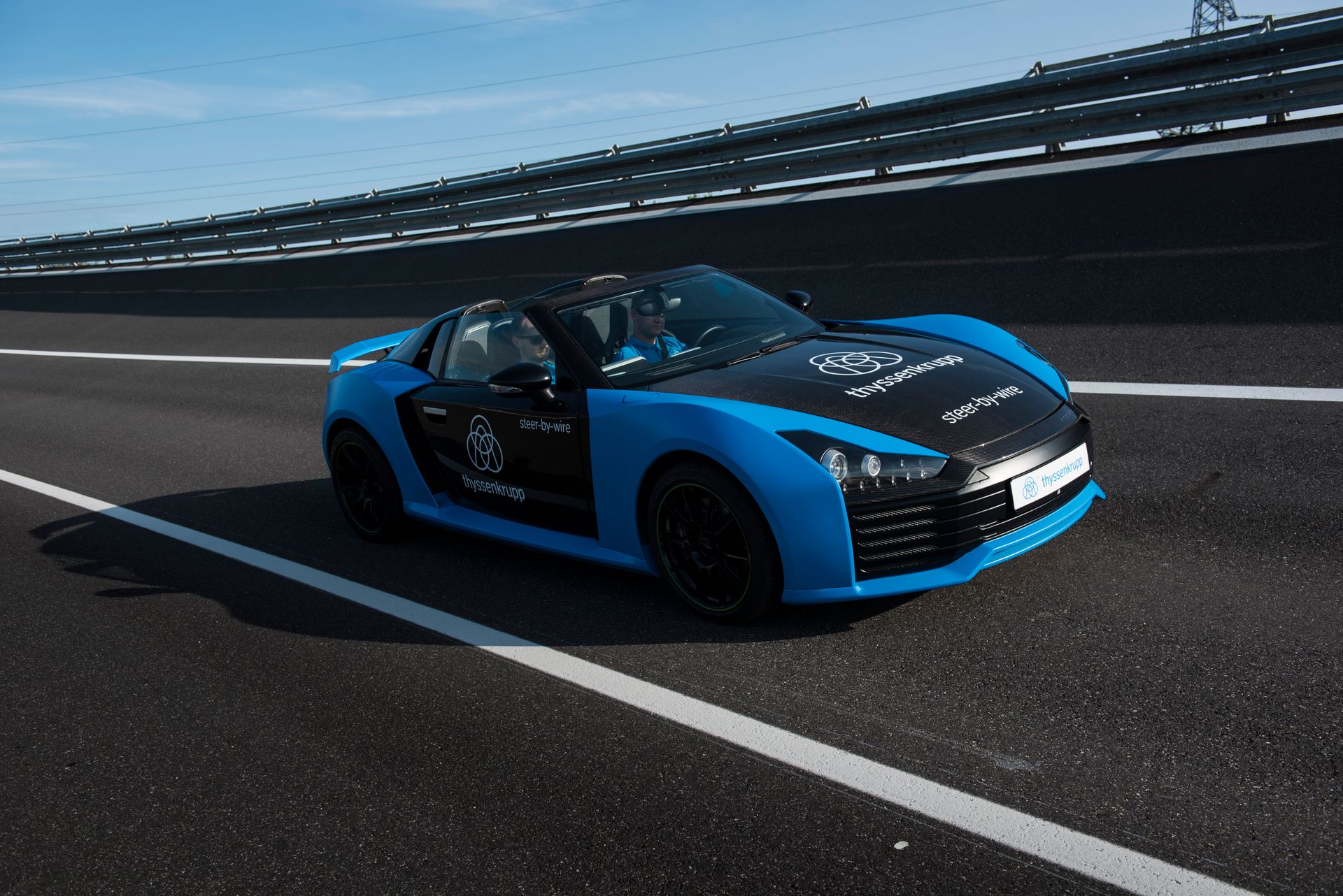 Ein blau-schwarzer Sportwagen mit thyssenkrupp Branding fährt auf einer Teststrecke. Das Fahrzeug steht für innovative Mobilitätslösungen und moderne Technologien für die Automobilindustrie.