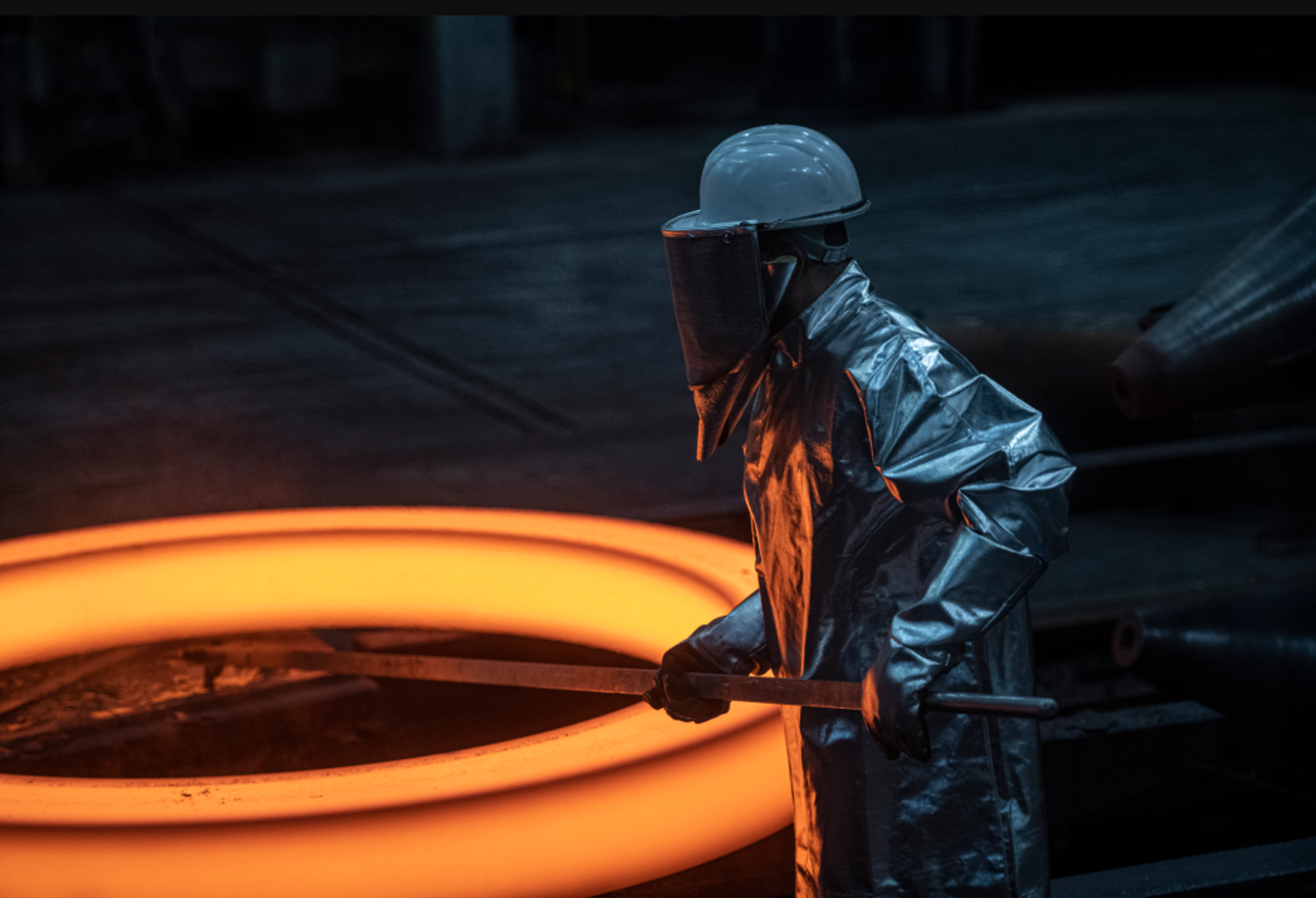 A worker in heat-resistant protective clothing handles a glowing hot steel ring at a thyssenkrupp production facility.
