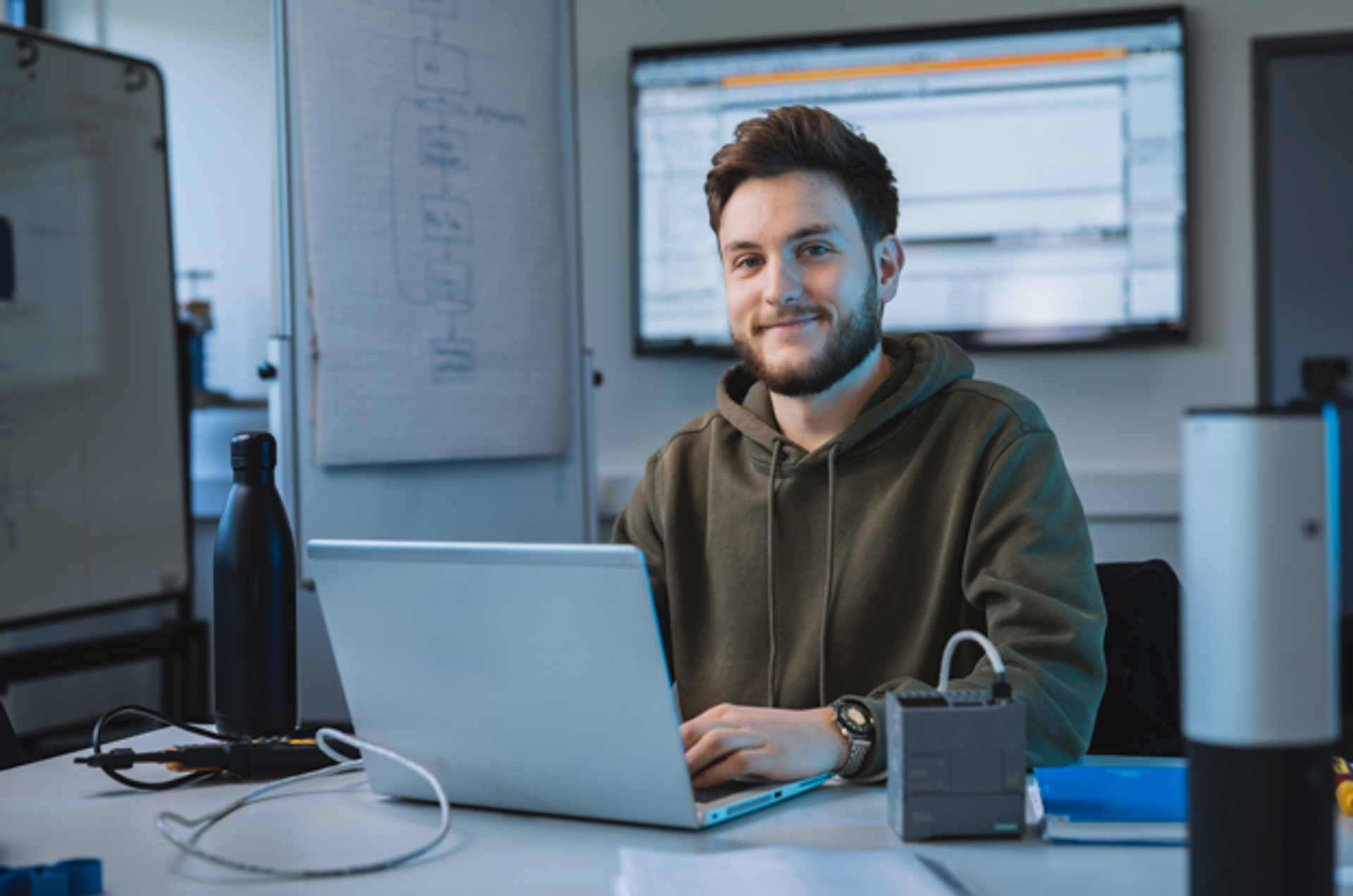 Ein Mann arbeitet am Laptop und ist von technischen Unterlagen und Geräten umgeben.