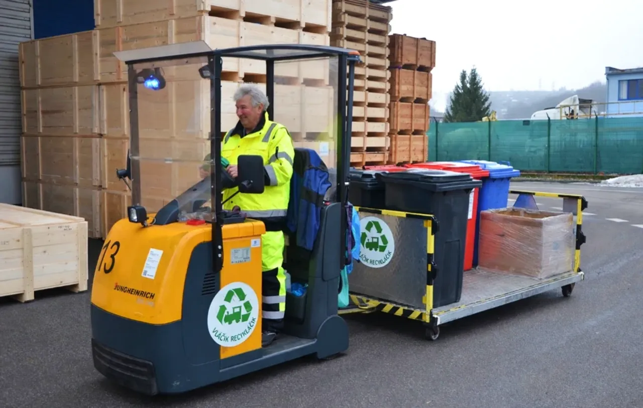 Man in yellow workgear driving a trolley with garbage cans