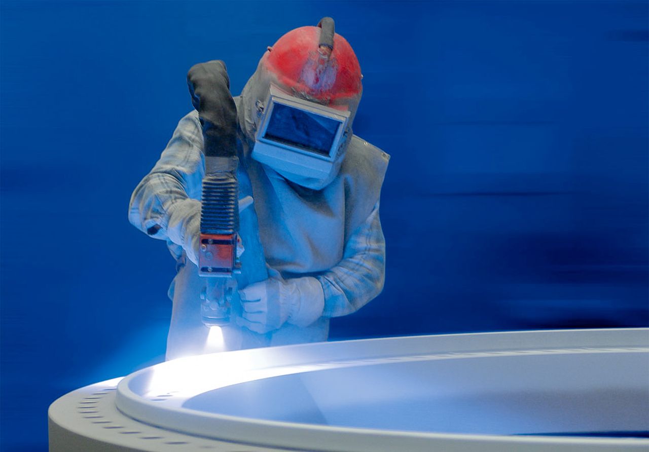 Man in a protective suit and helmet coats a slewing bearing