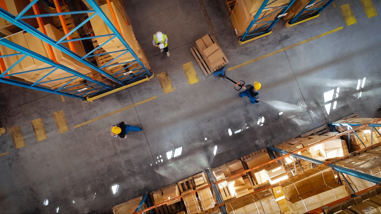 several workers in warehouse environment carrying out tasks based on logistics engineering priorities transferring boxes of parts to another area