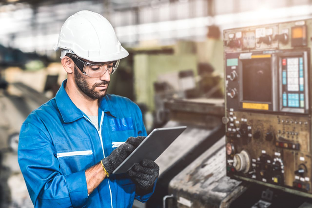 Anlagenbediener in Werkhalle analysiert Predictive Maintenance Informationen auf Tablet